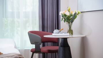 A hotel room with a bed, a red chair, a small round table with a vase of flowers, and a wall-mounted screen.