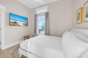 A bedroom with a bed, a window with curtains, a small stool, and a painting on the wall. - Topsail (Santa Rosa Beach)