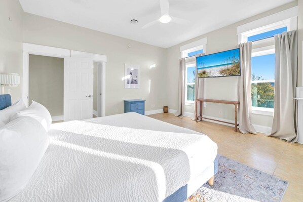 A bedroom with a large bed, a desk, a chair, a window with curtains, and a painting on the wall.