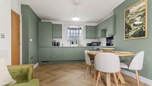 Una cocina moderna con armarios verdes, una mesa de comedor con sillas y piso de madera.