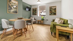 Una sala de estar moderna con un sofá verde, una mesa de comedor con sillas y obras de arte en las paredes.