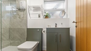 Baño con cabina de ducha de vidrio, inodoro, lavabo con espejo y un armario.