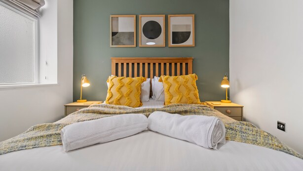 Una cama bien tendida con un edredón a rayas, dos lámparas de noche y un cabecero con diseño de listones de madera.