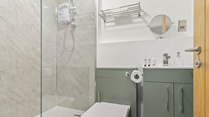 A bathroom with a glass shower enclosure, a white toilet, and a green cabinet with a mirror above it. - Pear Tree - BRAND NEW Stylish City Centre Apartment - Sleeps 3 (Worcestershire)