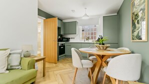 A modern kitchen with a dining area, a green sofa, and a wooden table. - Pear Tree - BRAND NEW Stylish City Centre Apartment - Sleeps 3 (Worcestershire)