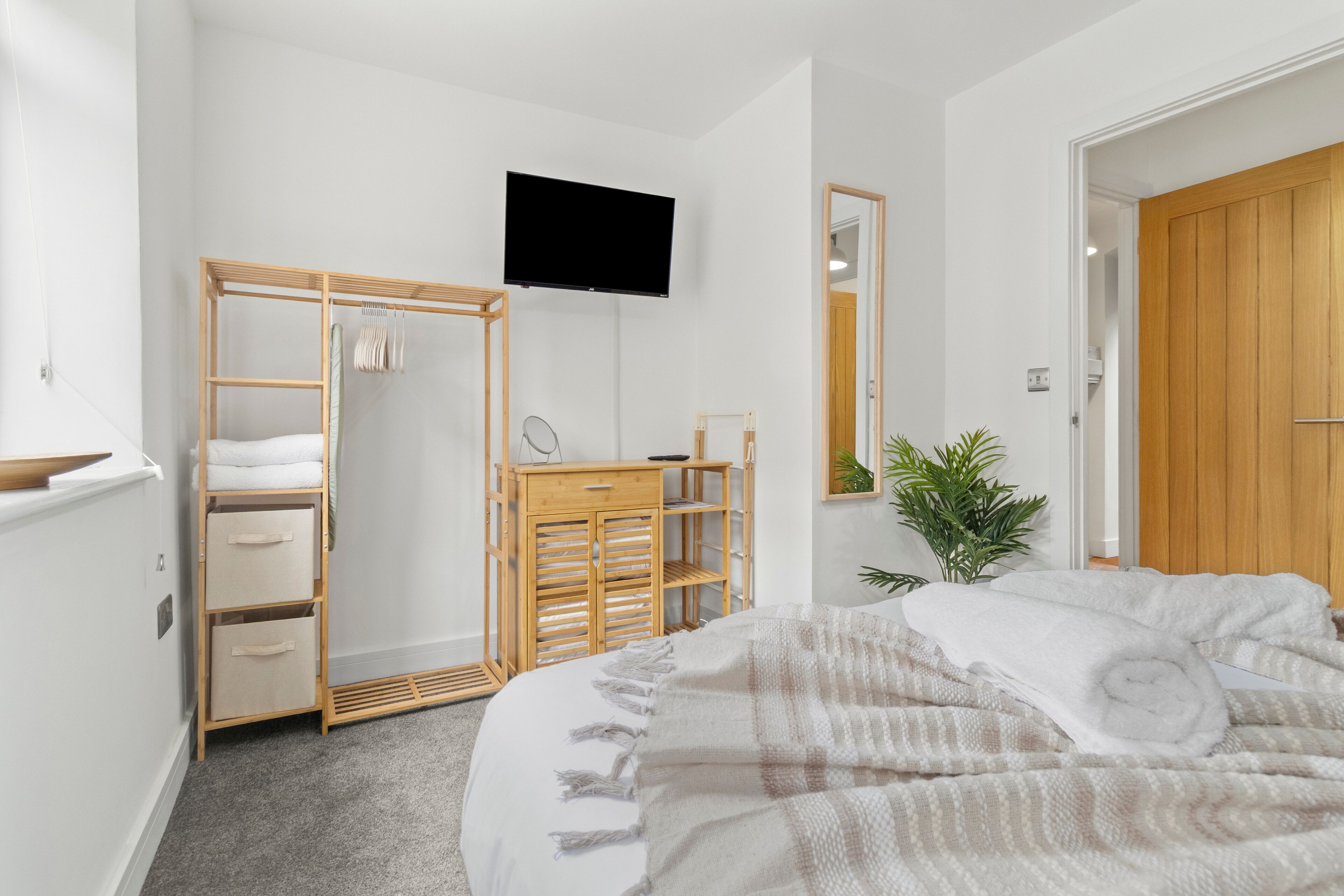 Quarto com cama, guarda-roupa de madeira, televisão, espelho e planta em vaso.