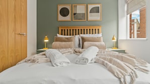 A neatly made bed with white linens and a beige throw blanket, two bedside lamps, and three framed artworks on the wall. - Pear Tree - BRAND NEW Stylish City Centre Apartment - Sleeps 3 (Worcestershire)