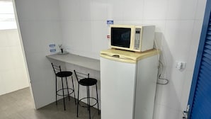 A compact kitchen with a microwave on top of a white refrigerator, two black bar stools, and a small countertop with a sink. - Studio em São Paulo - Expo Center Norte (São Paulo)
