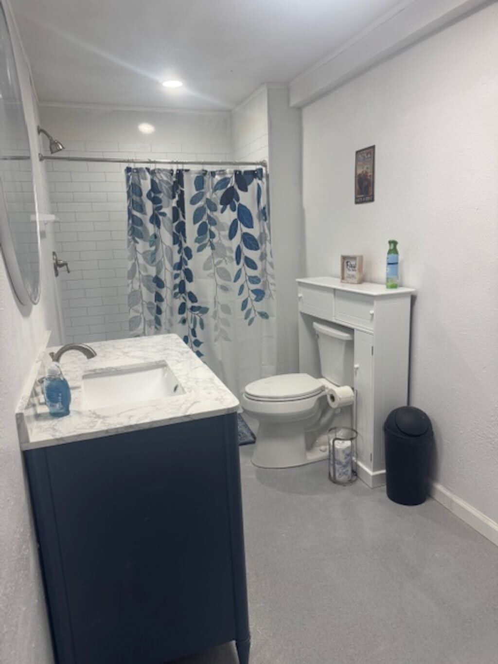 Een badkamer met een wit wastafelmeubel, toilet en douche met gordijn met bladmotief.