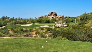 Un campo da golf con bunker sabbiosi, un bastone segnalino e un cielo azzurro limpido.