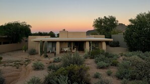 Una casa in stile desertico con tetto piatto, circondata da cactus e arbusti, sotto un cielo sereno.