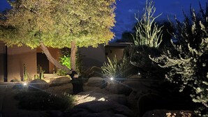 Un giardino curato con un grande albero, rocce e un edificio sullo sfondo.
