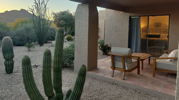 Un patio con un'area salotto, vista su un paesaggio desertico e un edificio con una porta vetrata che conduce a una camera da letto.