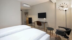 A hotel room with a bed, a desk, a chair, a TV, and a clock on the wall. - Nordic Hotel Lagos (Victoria Island)