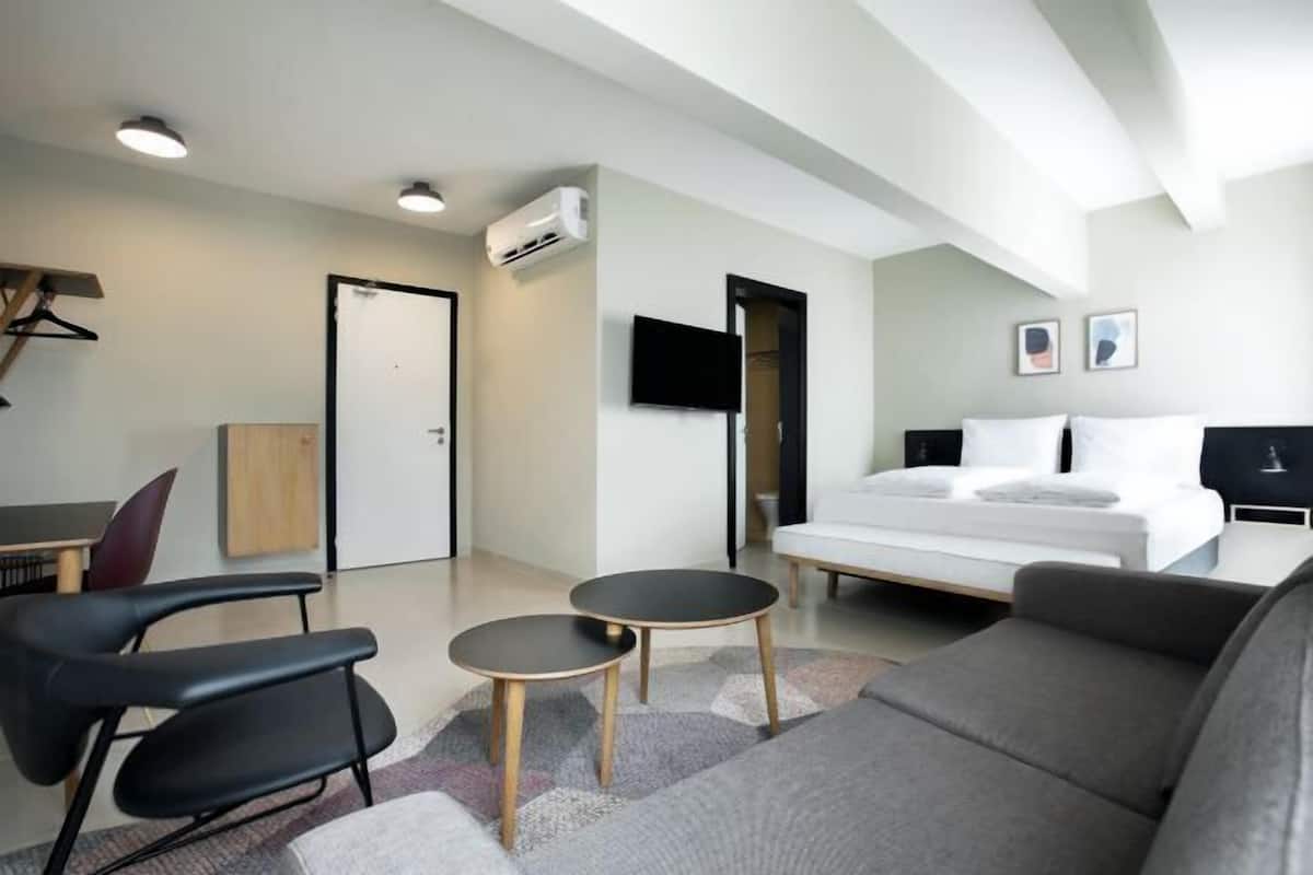 A modern hotel room with a bed, a desk, a chair, a TV, and an air conditioning unit.