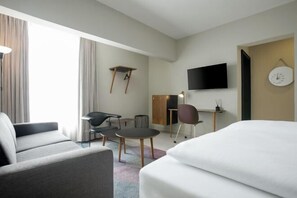 A hotel room with a bed, a sofa, a desk, a chair, a television, and a clock on the wall. - Nordic Hotel Lagos (Victoria Island)