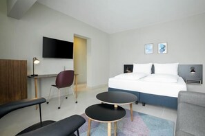A modern hotel room with a bed, a desk, a chair, a small table, and a TV. - Nordic Hotel Lagos (Victoria Island)