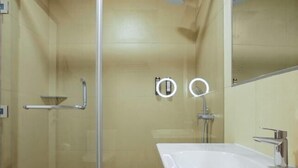 A bathroom with a glass shower enclosure, a white sink, and a mirror. - Nordic Hotel Lagos (Victoria Island)