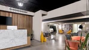 A modern reception area with a marble counter, wooden paneling, and a variety of seating options including yellow and orange chairs. - Nordic Hotel Lagos (Victoria Island)