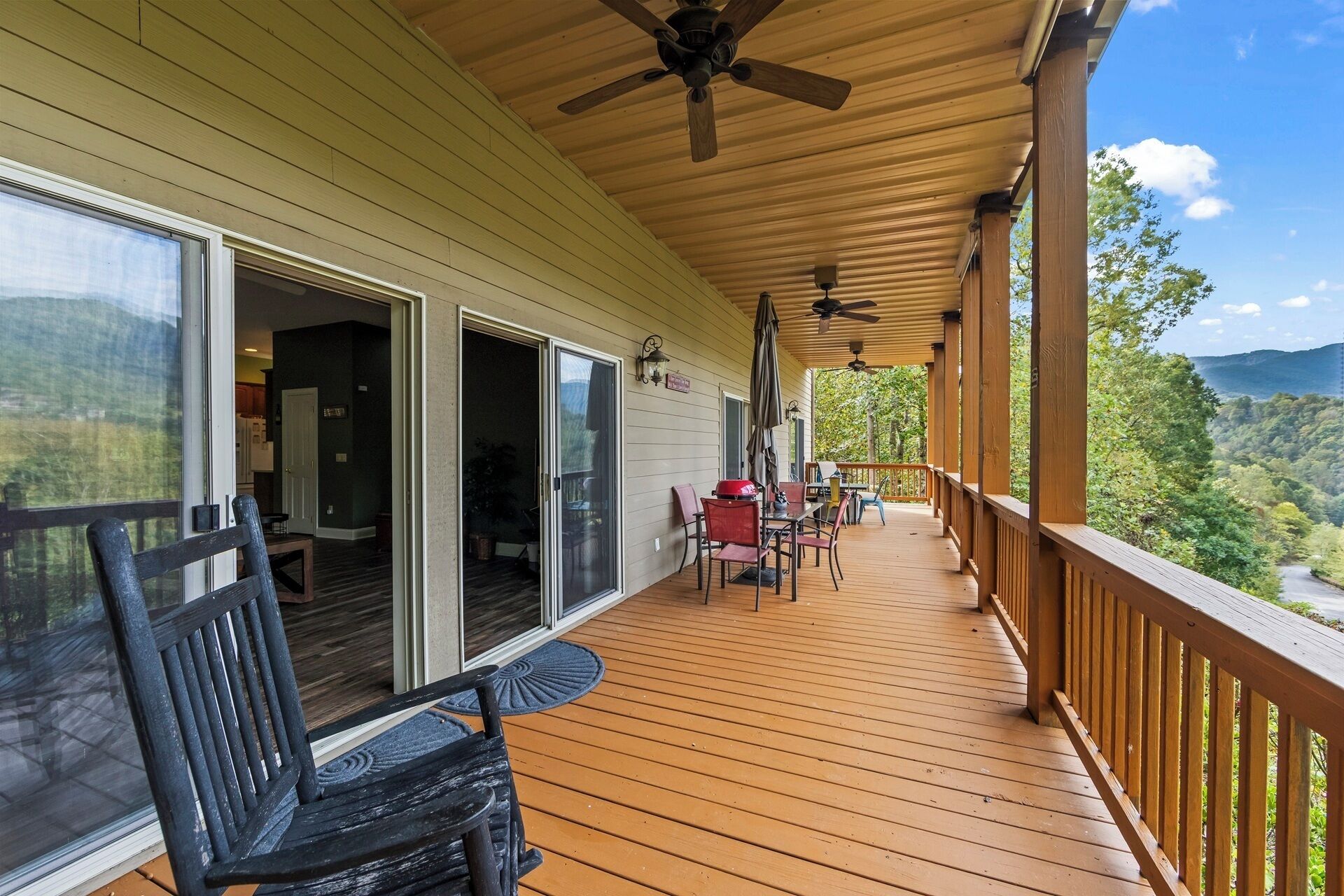 Une terrasse en bois dotée d’un espace abrité, de mobilier d’extérieur et offrant une vue panoramique sur une zone boisée.