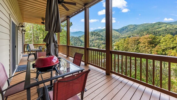 A covered outdoor deck with a table and chairs, overlooking a mountainous landscape.