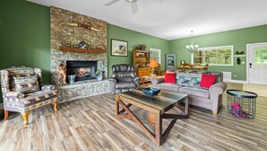 A living room with a stone fireplace, a ceiling fan, and a green wall.