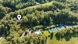 An aerial view of a property with a tennis court, a swimming pool, and a house surrounded by dense forest.