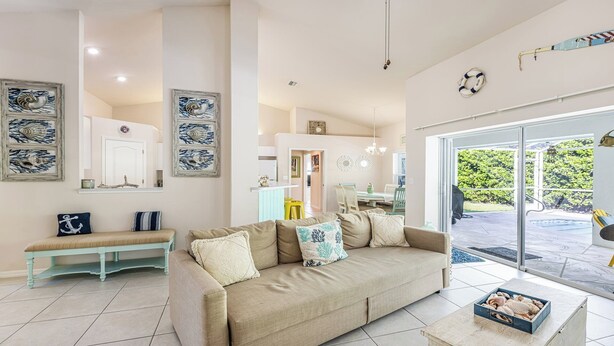 A spacious living room with a beige sofa, a bench, and nautical-themed wall art.