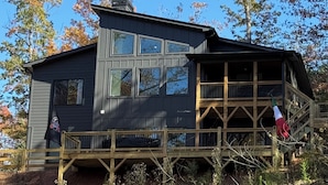 A two-story cabin with a balcony, surrounded by trees. - Lakefront home with Mountain Views (Mill Spring)