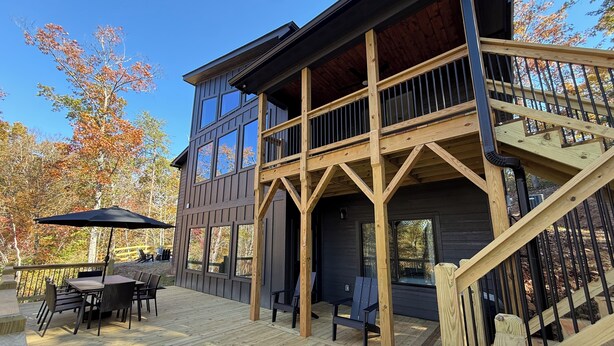 A two-story wooden cabin with a deck, outdoor seating, and a staircase. - Lakefront home with Mountain Views (Mill Spring)