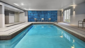 A modern indoor swimming pool with clear blue water, surrounded by a tiled deck and a blue curtain wall. - Candlewood Suites Chatham South by IHG (Chatham)