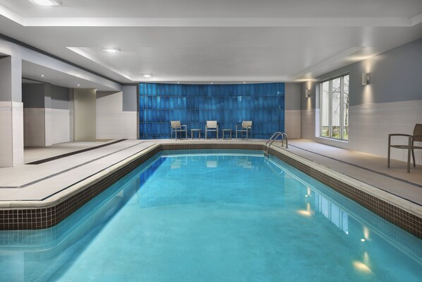 A modern indoor swimming pool with clear blue water, surrounded by a tiled deck and a blue curtain wall. - Candlewood Suites Chatham South by IHG (Chatham)