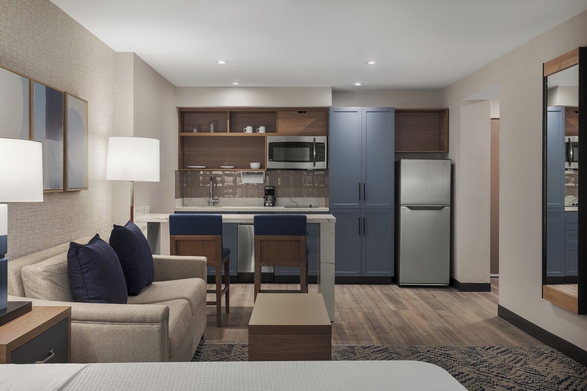 Una habitación de hotel moderna con kitchenette, sofá, mesa de comedor y cama.