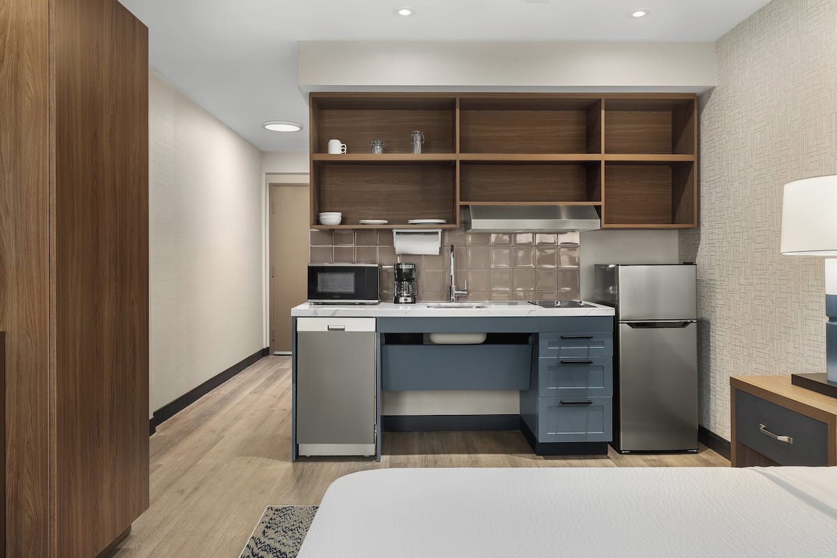 A compact hotel room with a kitchenette, including a microwave, coffee maker, sink, and refrigerator.
