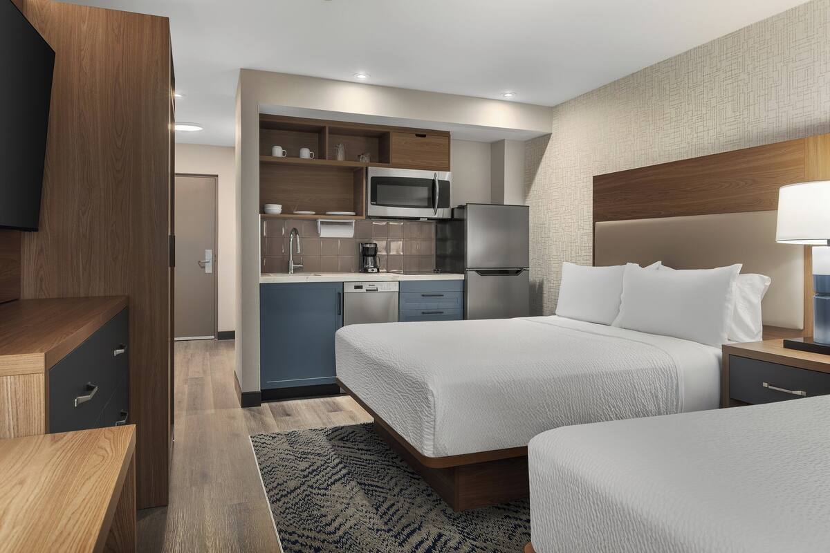 A hotel room with a bed, bedside table, and a built-in kitchen area including a microwave and refrigerator.
