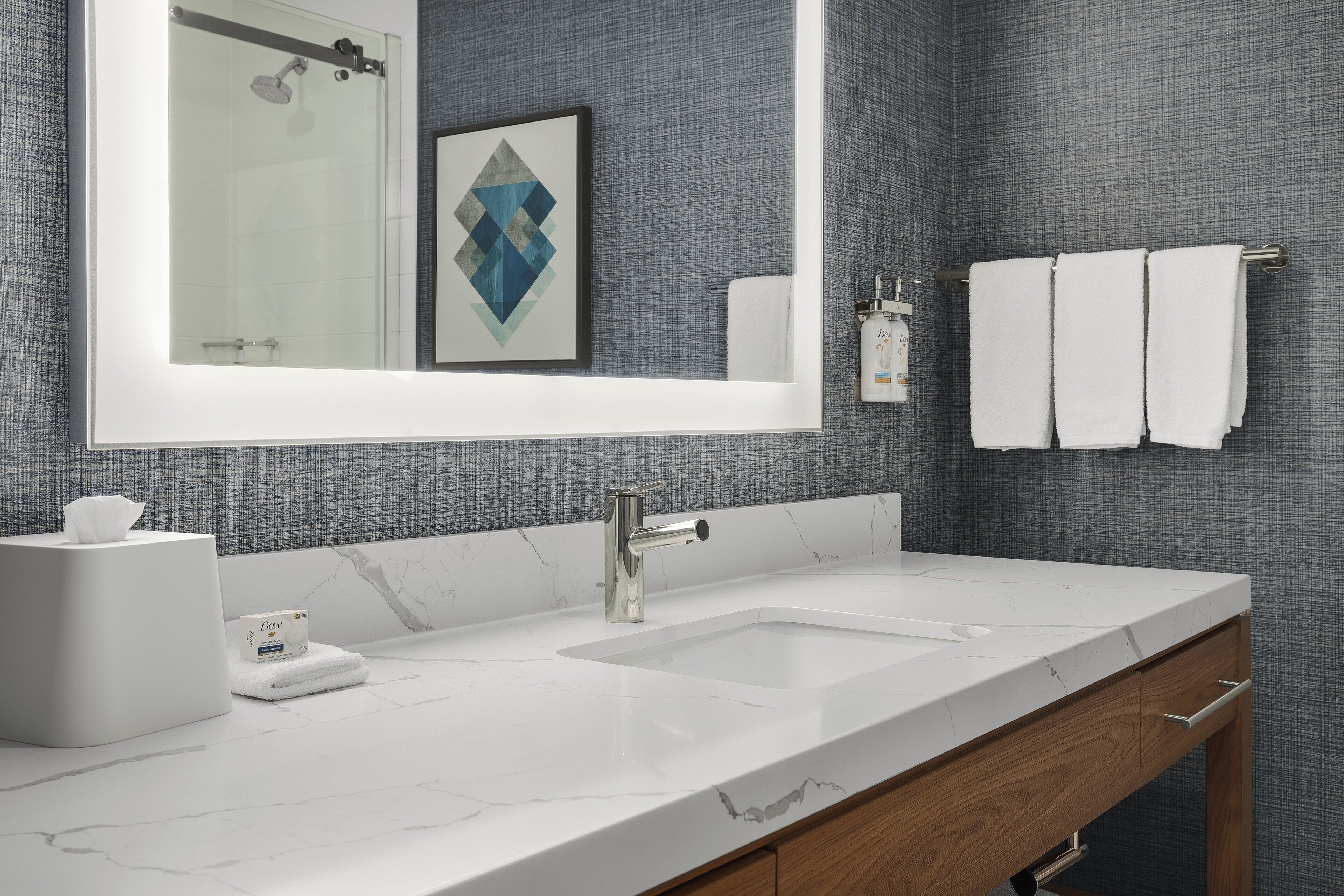 Un baño moderno con un espejo grande, un lavamanos blanco y un perchero para toallas.