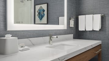 Un baño moderno con un espejo grande, un lavamanos blanco y un perchero para toallas.