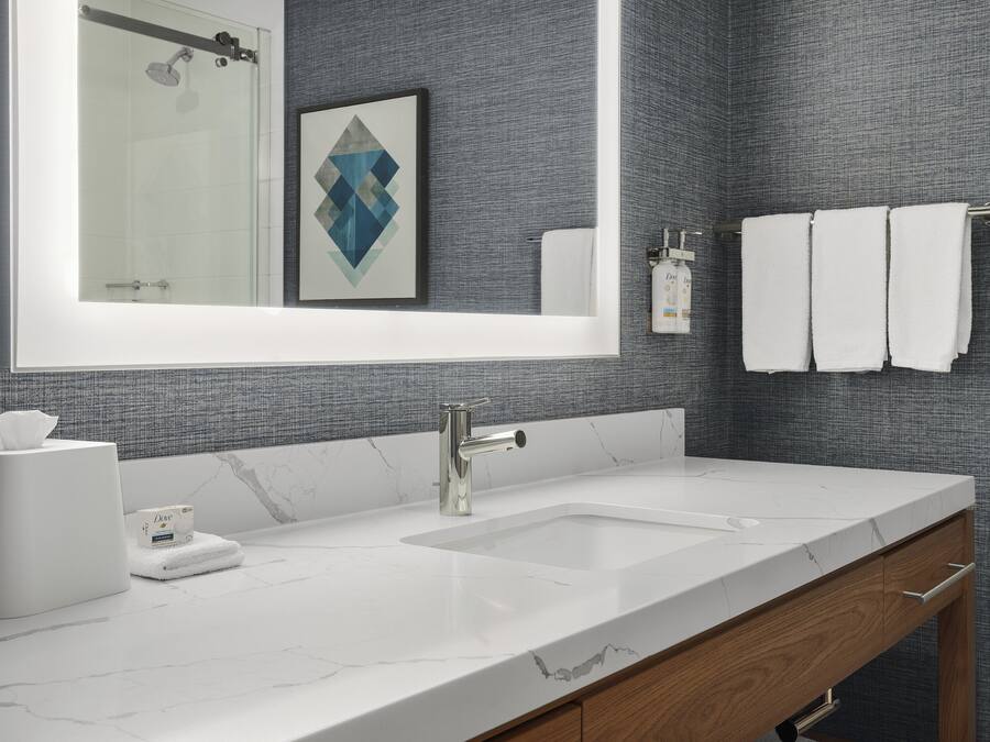 Un bany modern amb un mirall gran, un lavabo blanc i un penjador de tovalloles.