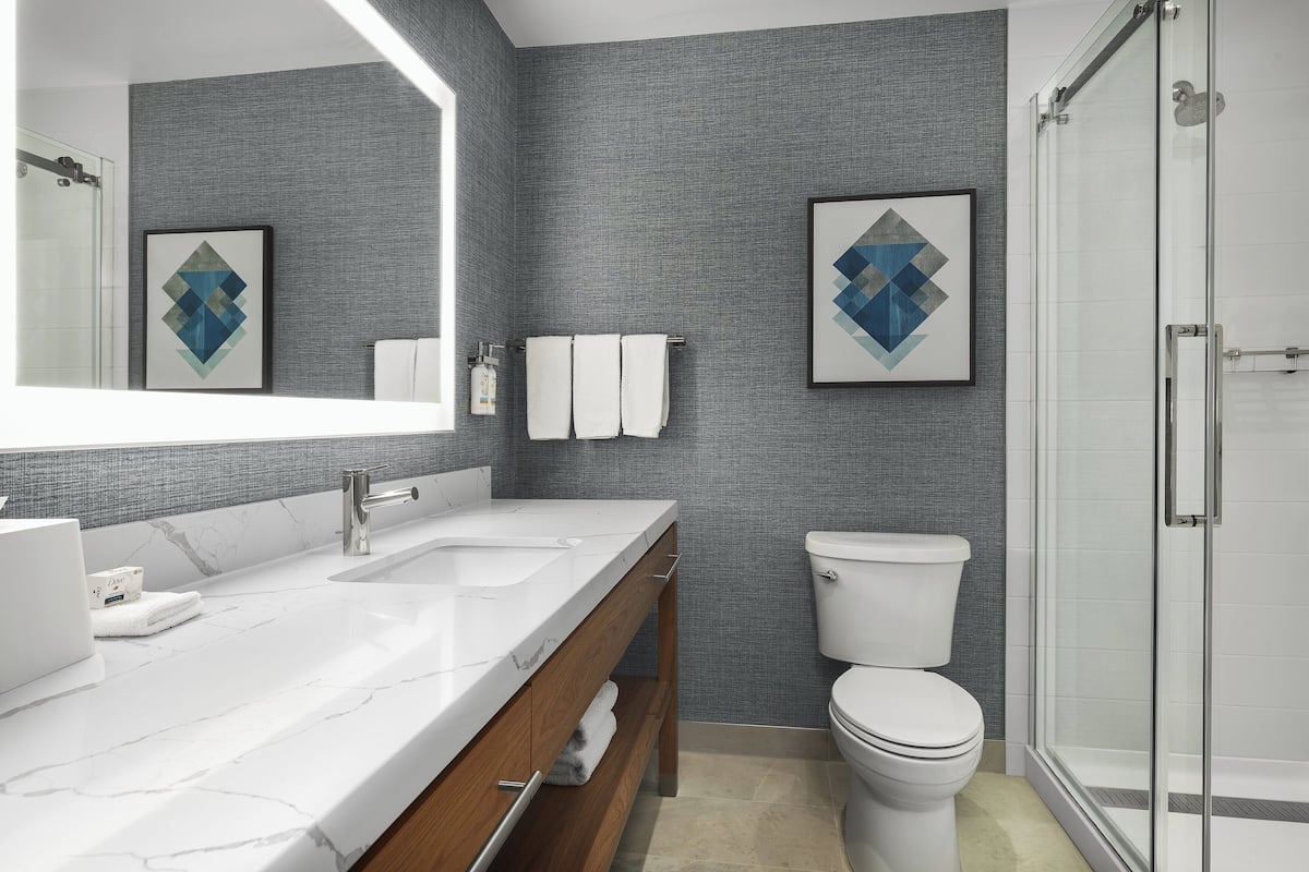 A modern bathroom with a marble vanity, a toilet, and a glass shower enclosure.