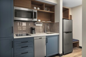 Una cocina moderna con electrodomésticos de acero inoxidable, armarios grises y un estante de madera.