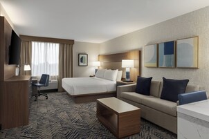 Una habitación de hotel con cama, escritorio, silla, sofá y televisión.