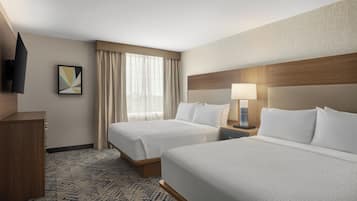 A hotel room with two beds, a wooden headboard, a flat-screen TV, a painting, and a window with curtains.