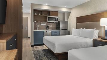 A hotel room with a bed, bedside table, and a built-in kitchen area including a microwave and refrigerator.