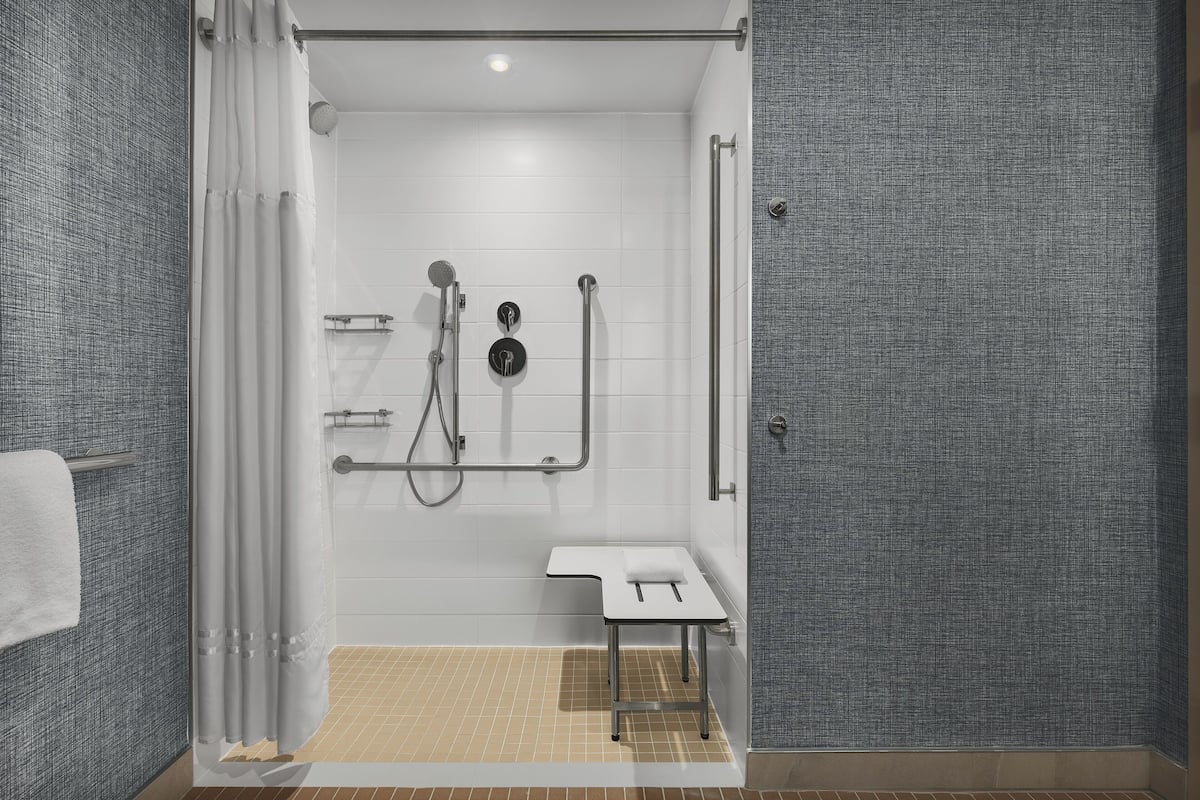 A modern bathroom with a shower, grab bar, and a small bench.