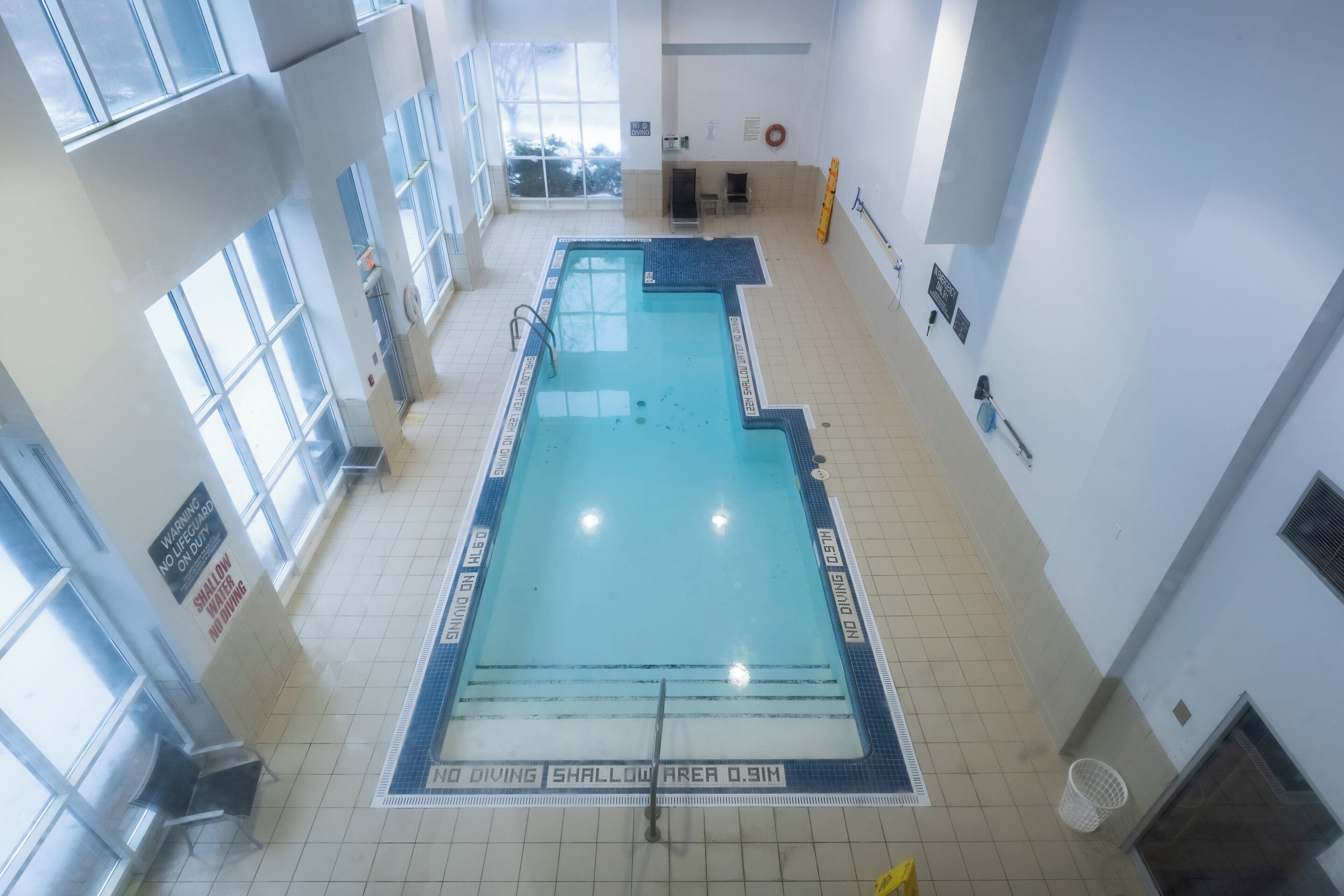 An indoor swimming pool with clear signage, tiled flooring, and a view of the outside through large windows.