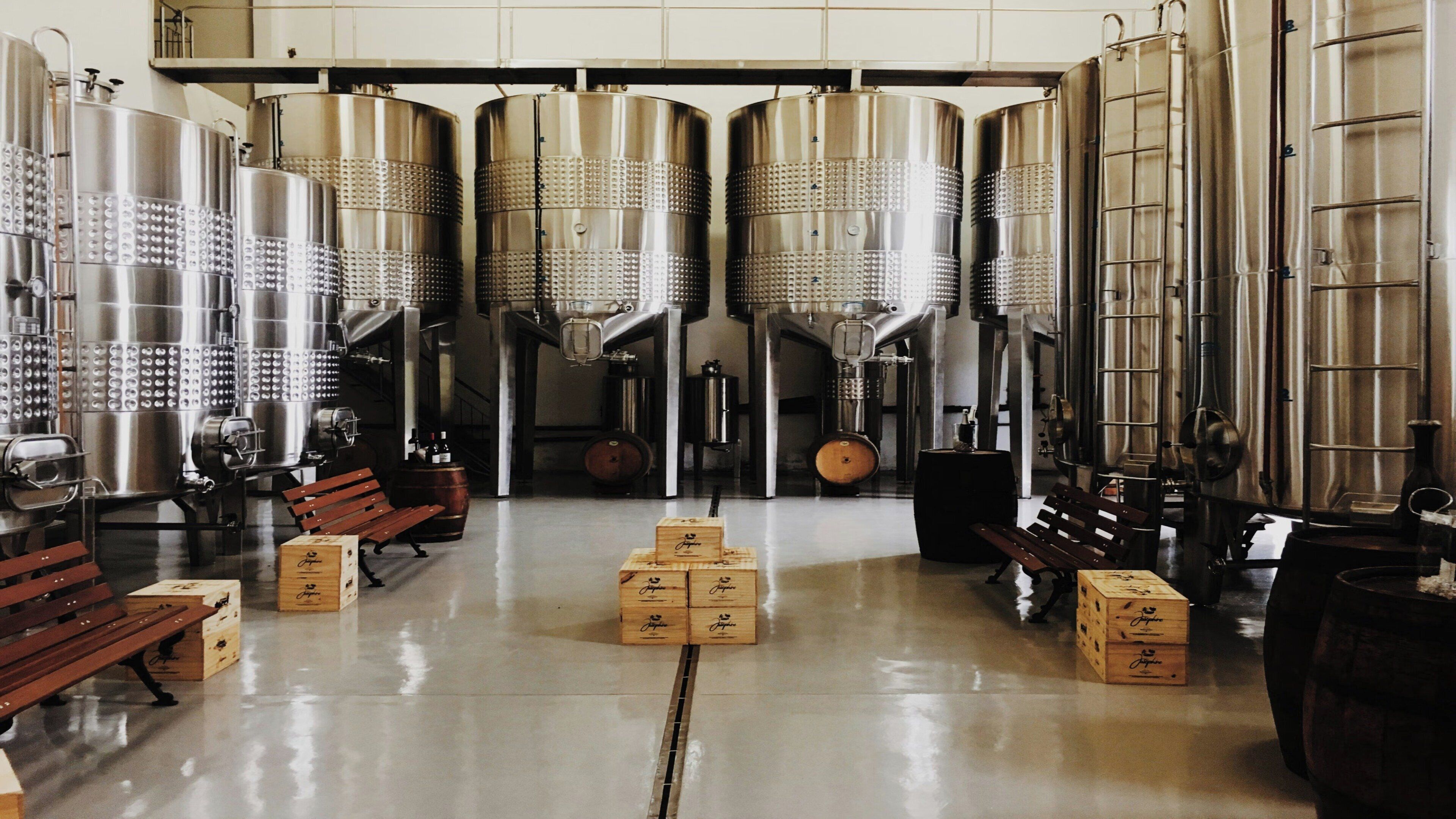 A clean, industrial-style room with stainless steel tanks, wooden crates, and benches.