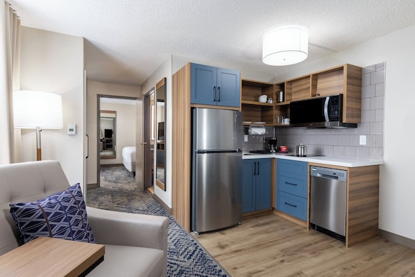 A compact kitchen with a refrigerator, microwave, and dishwasher. There is a seating area with a sofa and a small table. - Candlewood Suites London South by IHG (London)