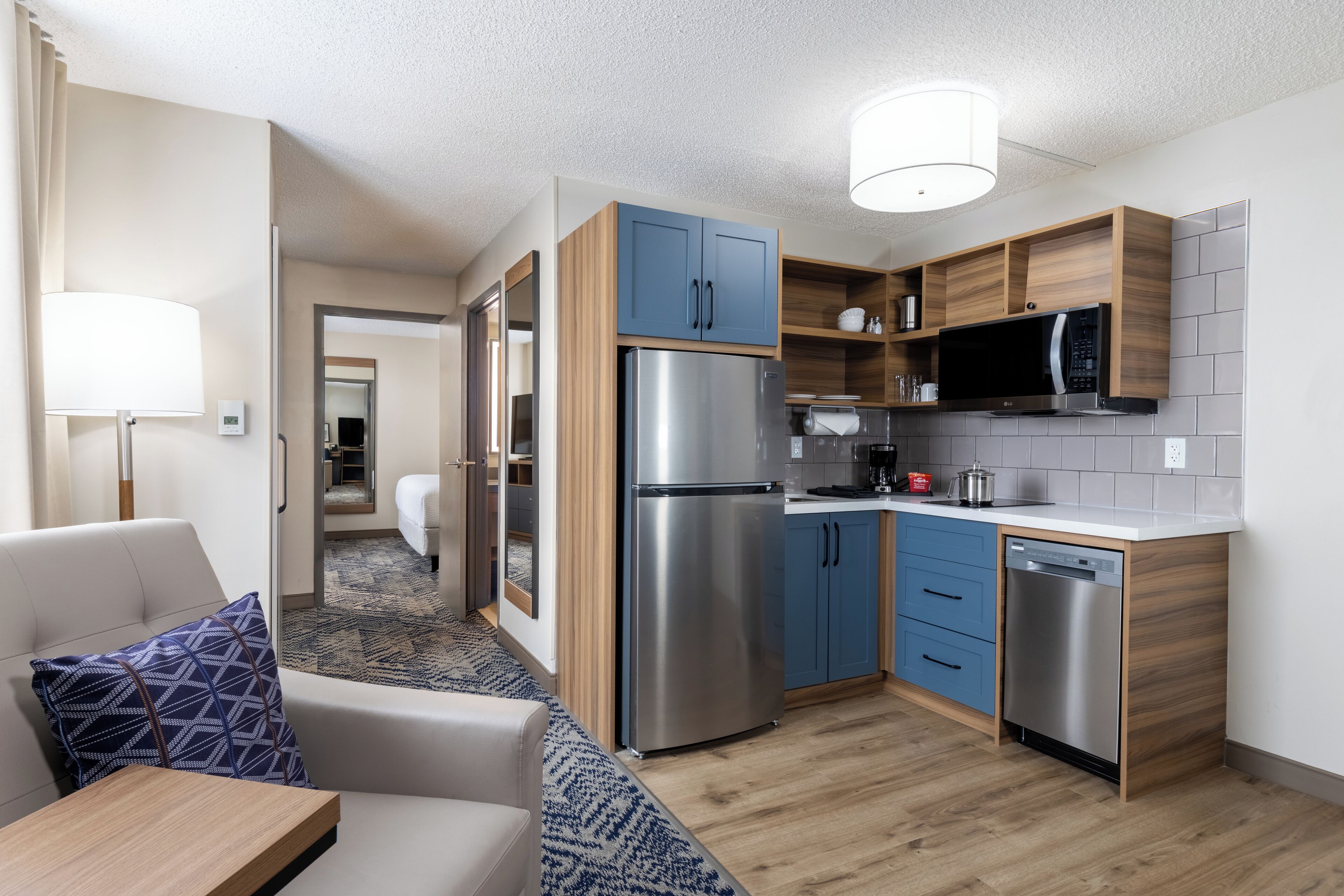 A modern kitchen with built-in appliances, a dining area with a sofa and table, and a hallway leading to a bedroom.