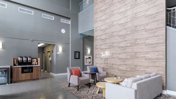 A spacious lobby with a modern design, featuring a seating area with sofas and armchairs, a coffee station, and a large wooden accent wall. - Candlewood Suites London South by IHG (London)