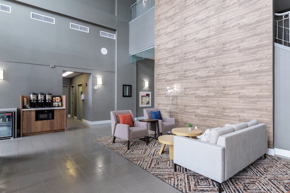 A spacious lobby with a modern design, featuring a seating area with sofas and armchairs, a coffee station, and a large wooden accent wall.